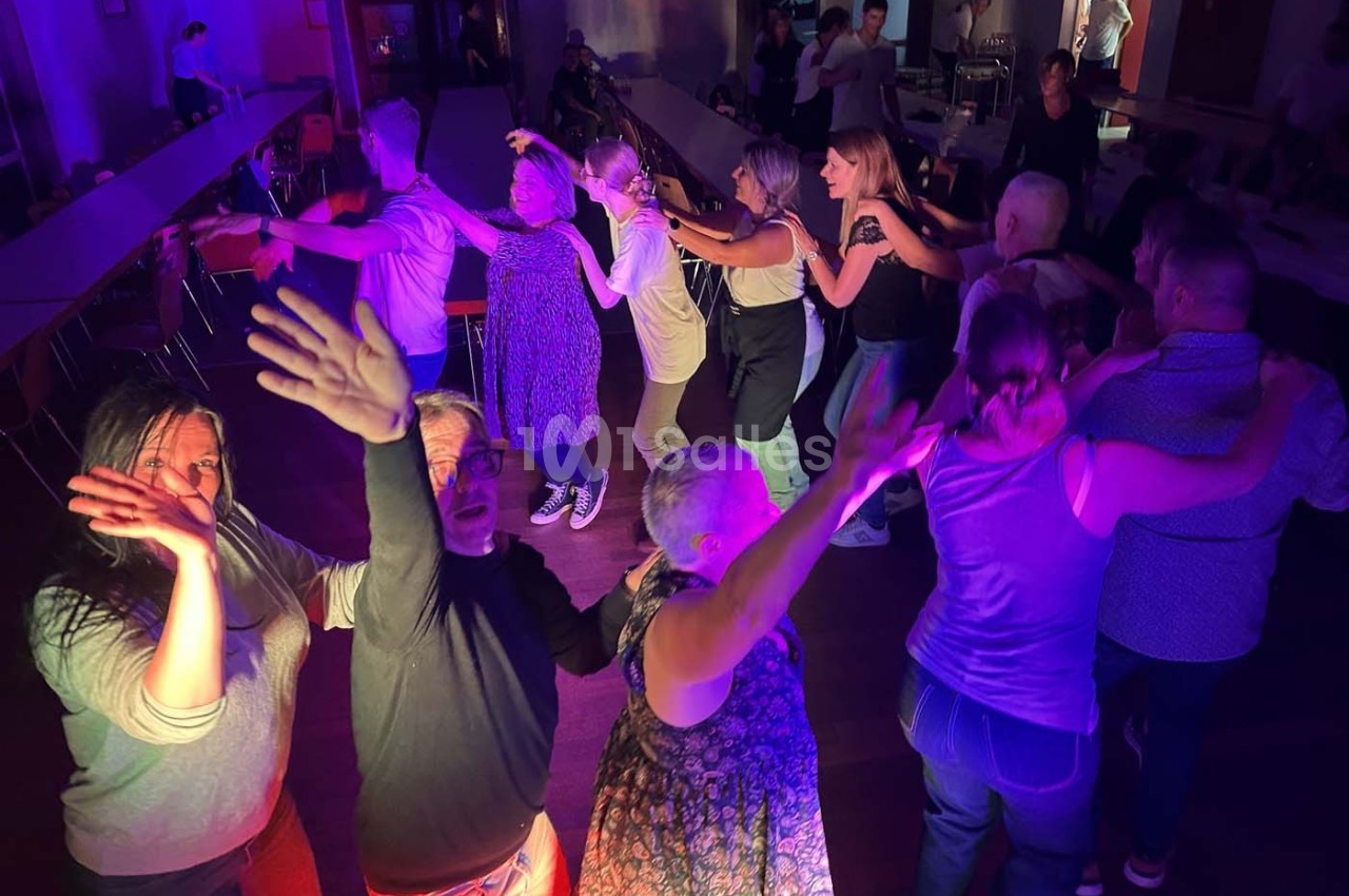 Des personnes dansent en groupe dans une salle éclairée par des lumières colorées, créant une ambiance festive.