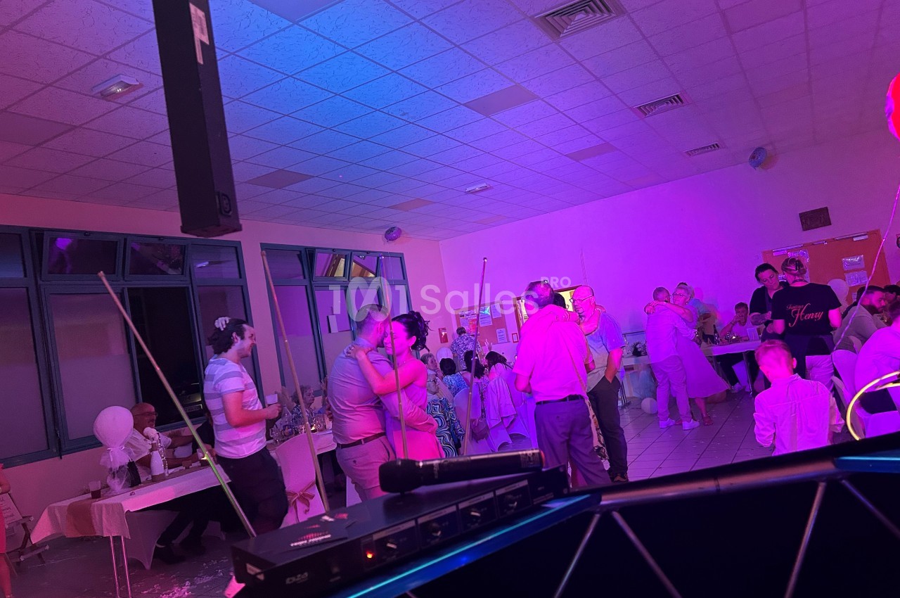 Des personnes dansent et discutent dans une salle éclairée par des lumières colorées lors d'un événement festif.