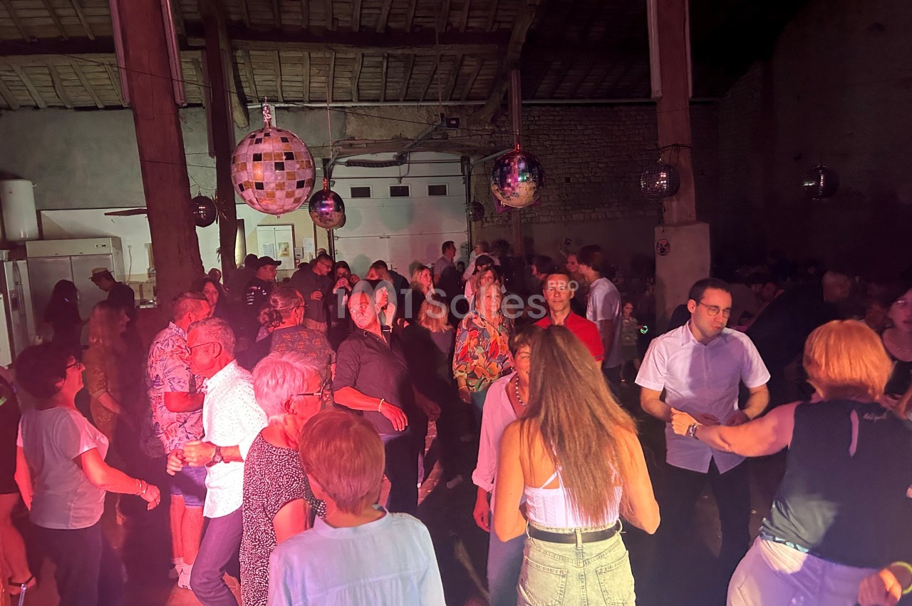 Des personnes dansent et discutent dans une salle éclairée par des lumières colorées et des boules à facettes.