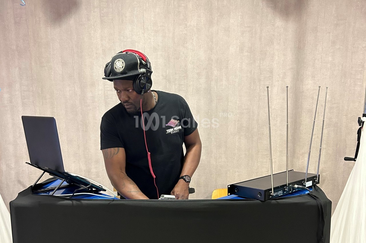 Un DJ mixe de la musique sur un ordinateur portable, équipé d'un casque, devant une table avec du matériel audio.