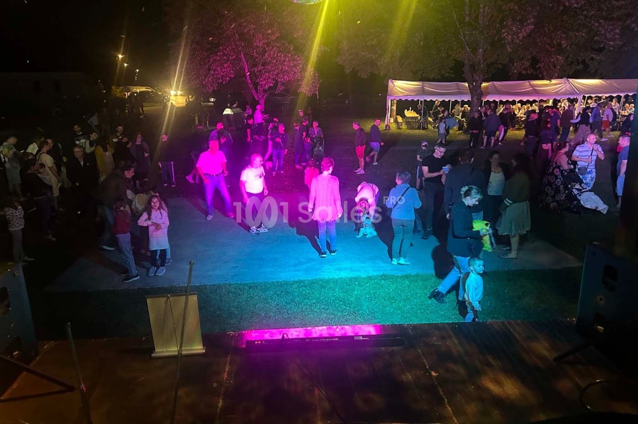 Des personnes dansent et se rassemblent sous des éclairages colorés lors d'un événement en plein air, de nuit.