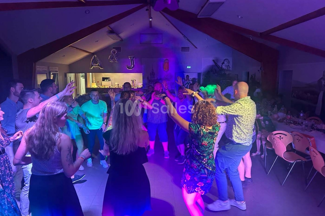 Des personnes dansent dans une salle éclairée par des lumières colorées, avec des décorations en arrière-plan.