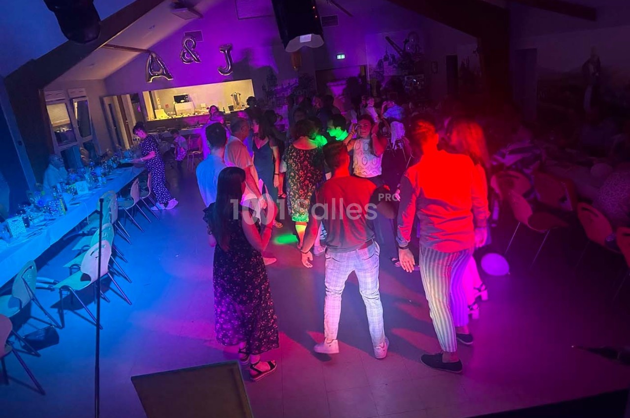 Des personnes dansent sous des lumières colorées dans une salle décorée, avec des tables disposées sur les côtés.
