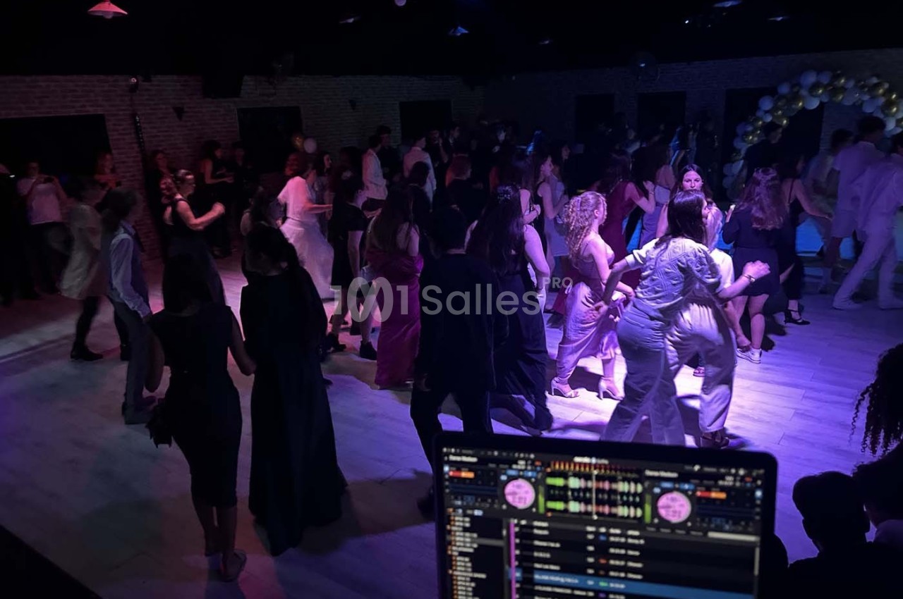 Groupe de personnes dansant dans une salle sombre avec un écran de mixage de DJ visible au premier plan.