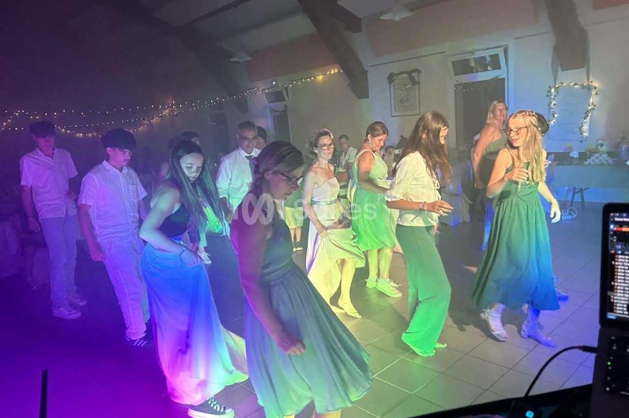 Des personnes dansent en groupe dans une salle éclairée par des lumières colorées, ambiance festive et décontractée.