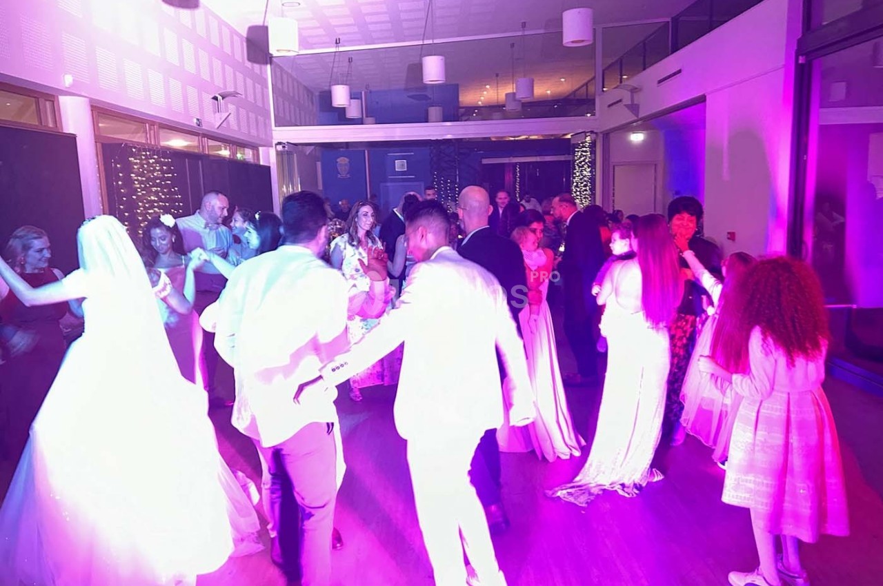 Des invités dansent dans une salle éclairée de lumières colorées, lors d'une fête ou d'une célébration.