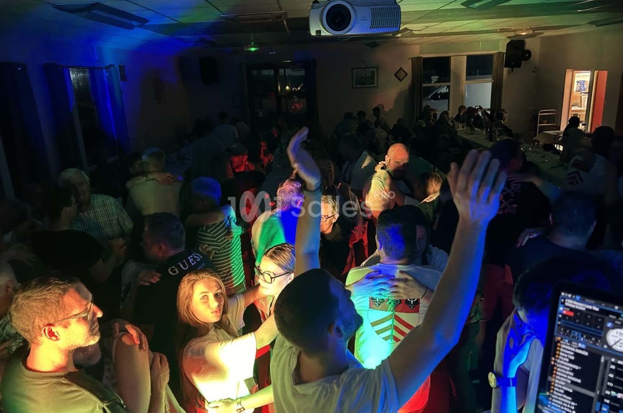 Groupe de personnes dansant et socialisant dans une salle éclairée par des lumières colorées.