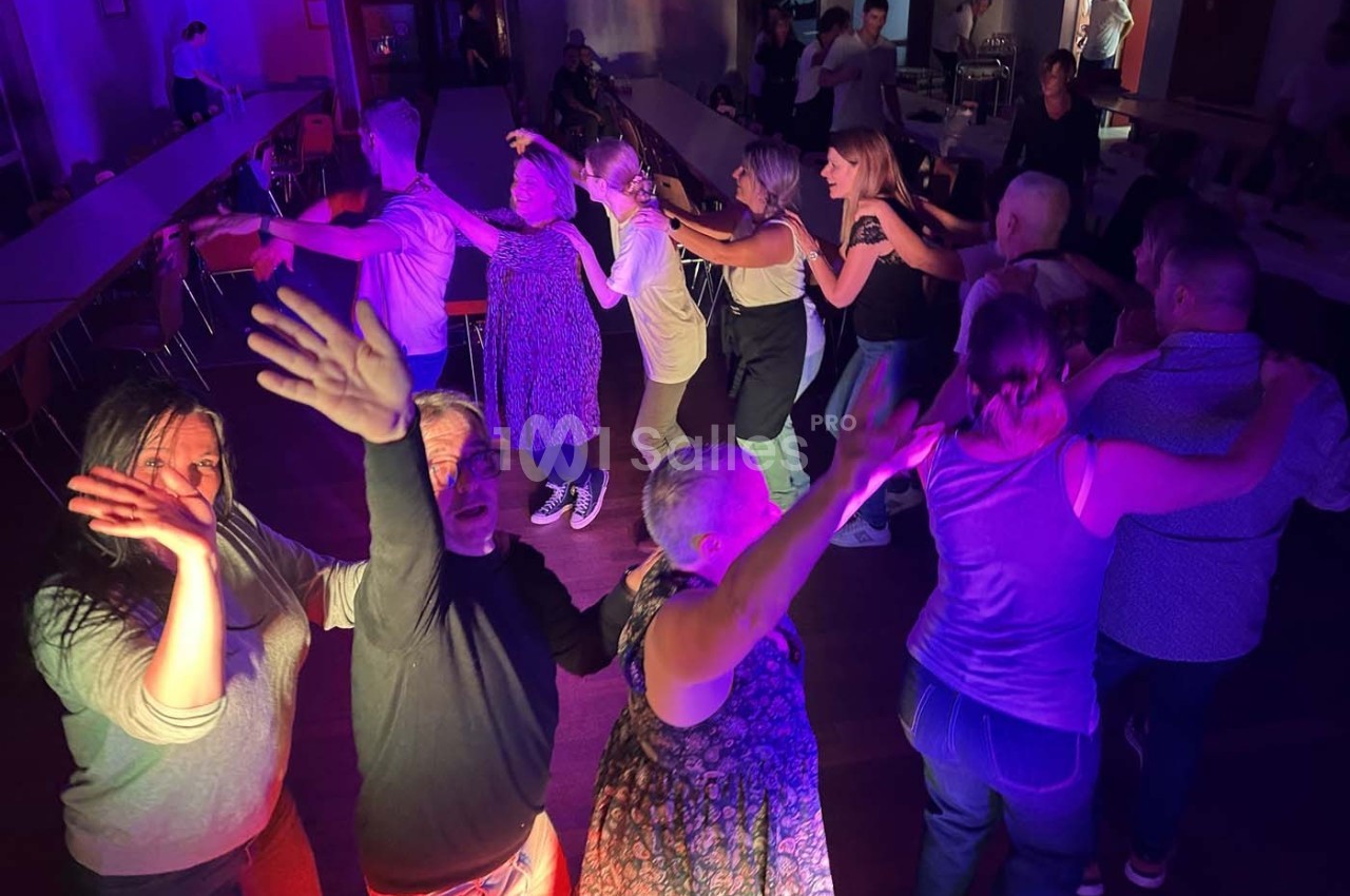Des personnes dansent en groupe dans une salle éclairée par des lumières colorées, créant une ambiance festive.
