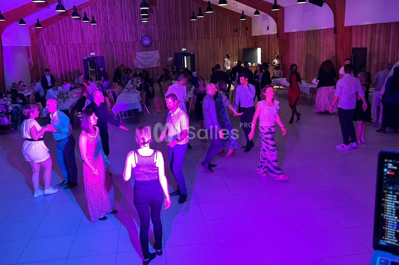 Des personnes dansent dans une salle éclairée de lumières colorées, avec des tables dressées en arrière-plan.