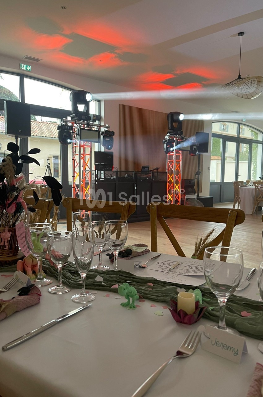 Salle de réception décorée pour un événement, avec tables dressées et une piste de danse équipée de lumières colorées.