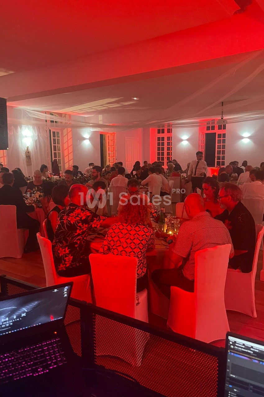 Salle de réception éclairée en rouge, avec des invités assis à des tables décorées, lors d'un événement festif.