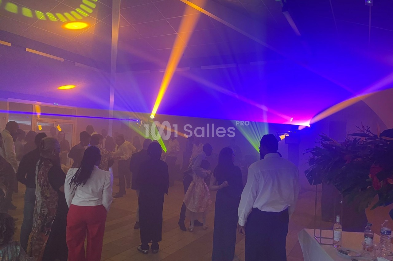 Des personnes dansent dans une salle éclairée par des jeux de lumière colorés, avec une ambiance festive.