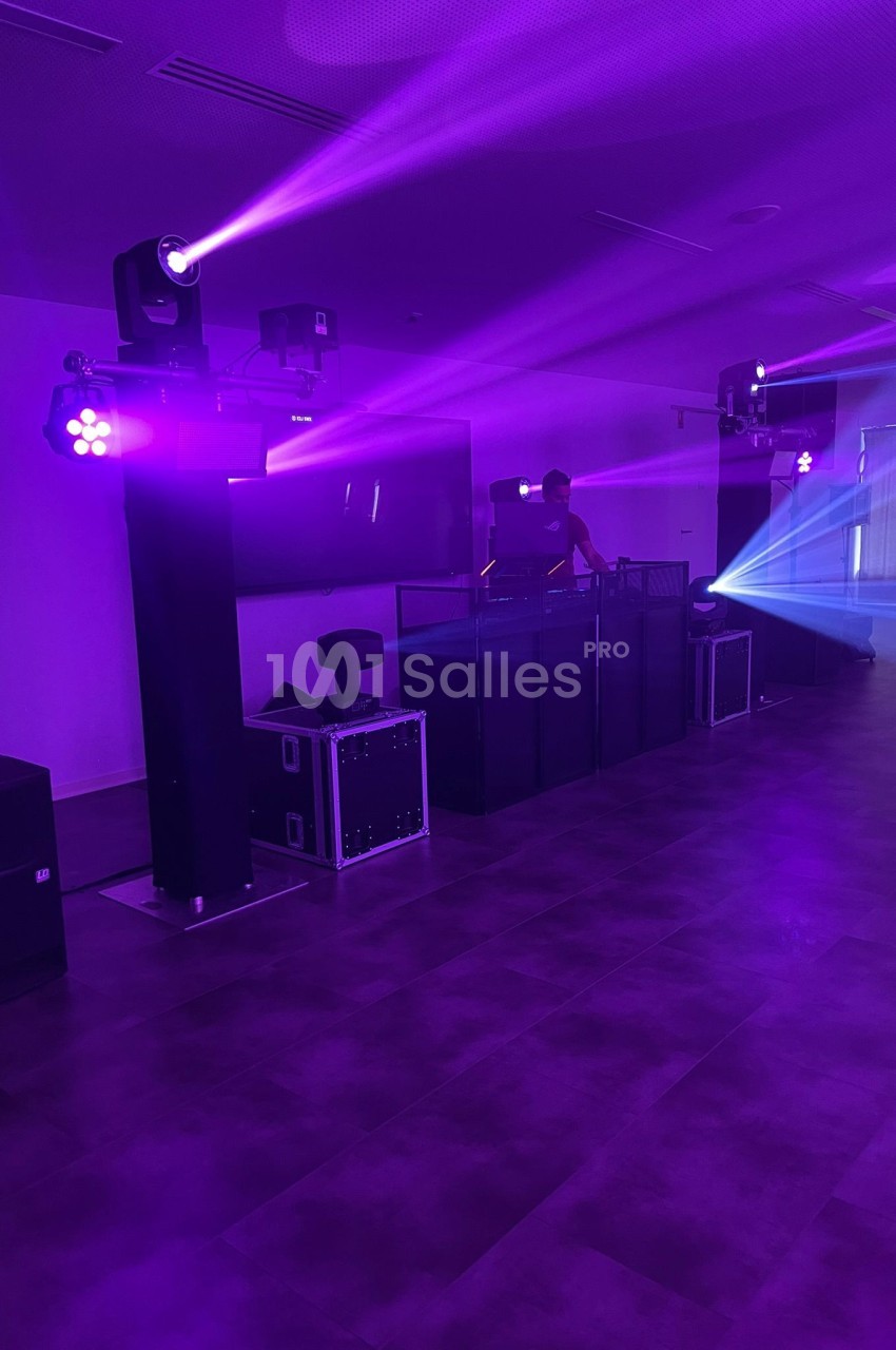 Salle sombre avec éclairage violet, un DJ derrière une table de mixage et des projecteurs diffusant des faisceaux lumineux.