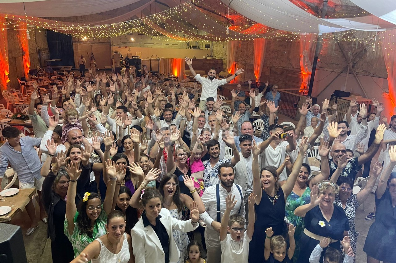 Groupe de personnes souriantes levant les bras dans une grande salle décorée avec des guirlandes lumineuses.