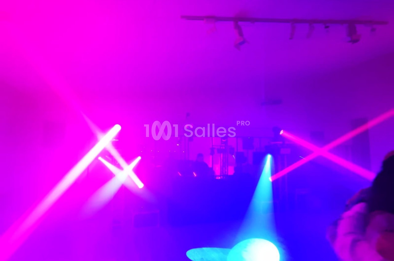 Salle sombre éclairée par des lumières colorées violettes et bleues, avec des projecteurs et une ambiance festive.