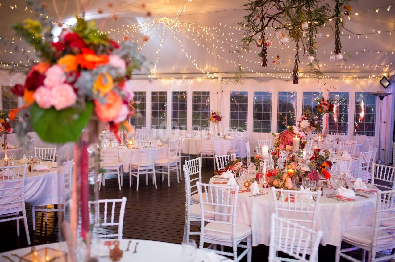 Salle de réception décorée avec des guirlandes lumineuses, des tables élégantes et des arrangements floraux colorés.