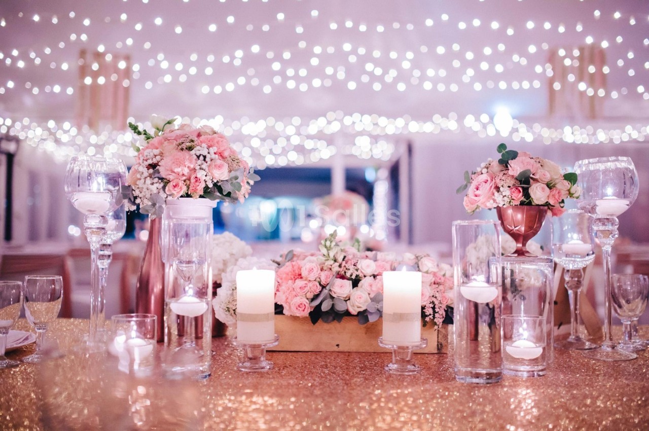 Décoration de table élégante avec bougies, fleurs roses et blanches, sous un plafond illuminé de guirlandes lumineuses.