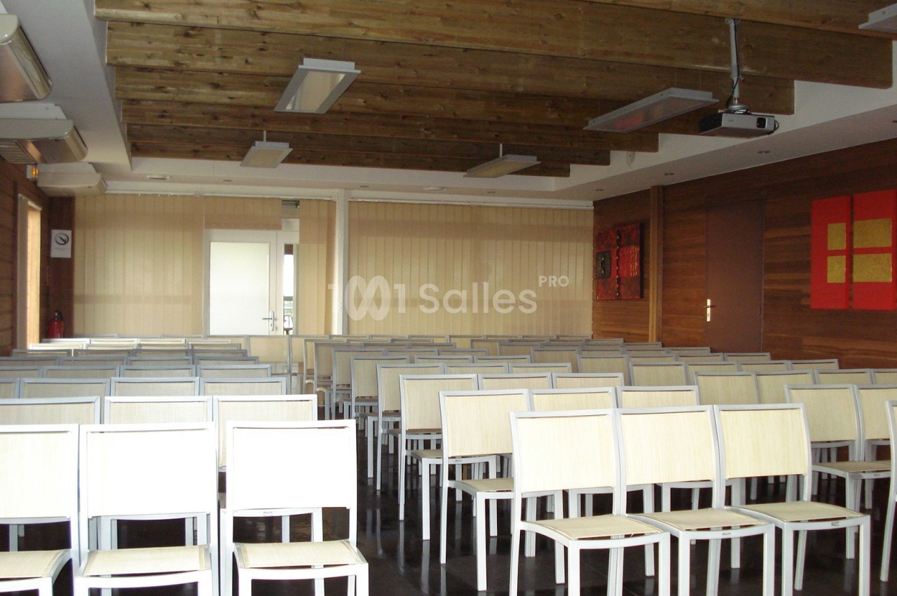 Salle de conférence vide avec des rangées de chaises blanches et un plafond en bois.