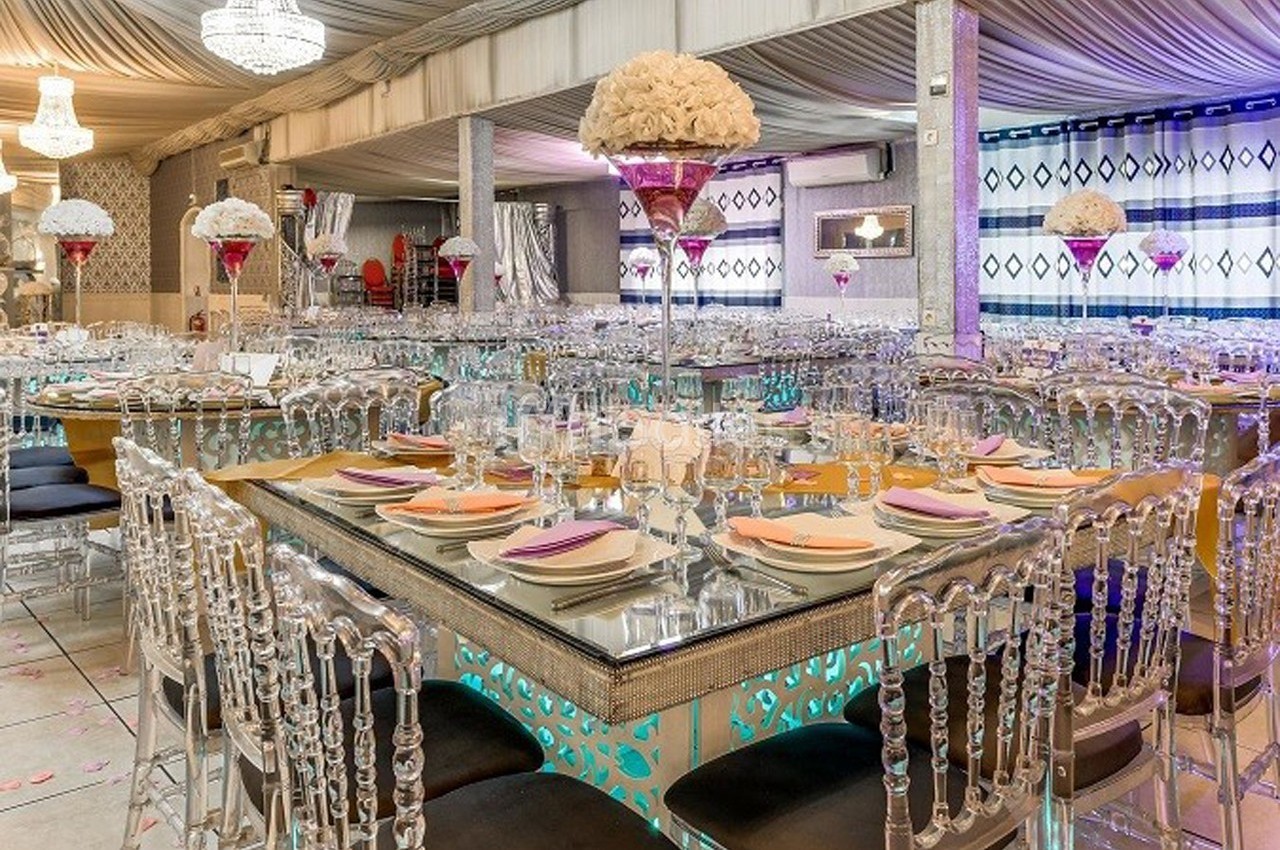 Salle de réception élégante avec tables en miroir, chaises transparentes et décorations florales raffinées.