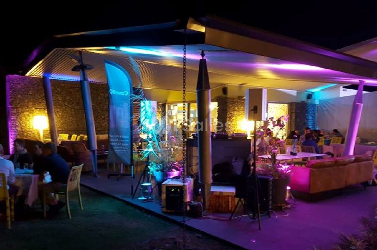 Terrasse éclairée de nuit avec des lumières colorées, des tables occupées et un bar en arrière-plan.