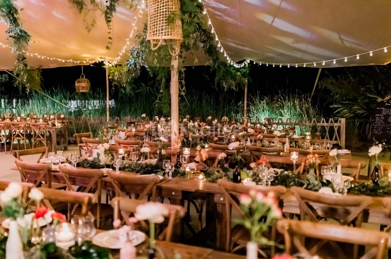 Salle de réception en plein air décorée de guirlandes lumineuses, tables en bois et arrangements floraux.
