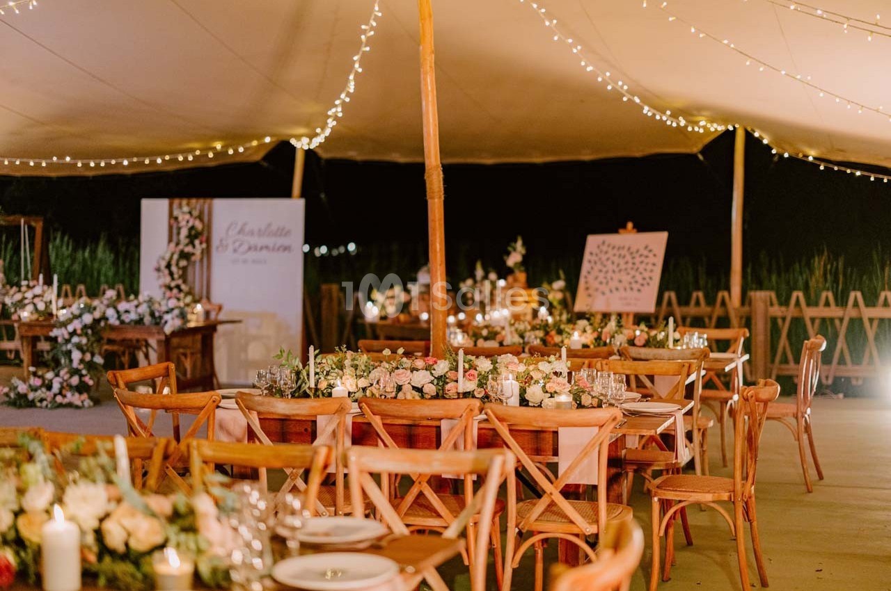 Salle de réception en plein air décorée de guirlandes lumineuses, tables en bois et arrangements floraux élégants.