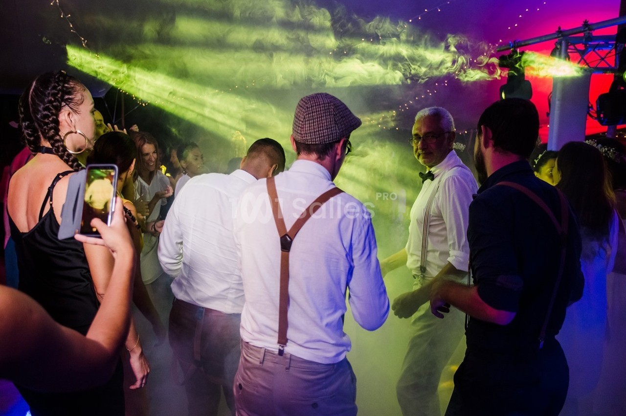 Groupe de personnes dansant sous des lumières colorées et de la fumée lors d'une soirée festive.