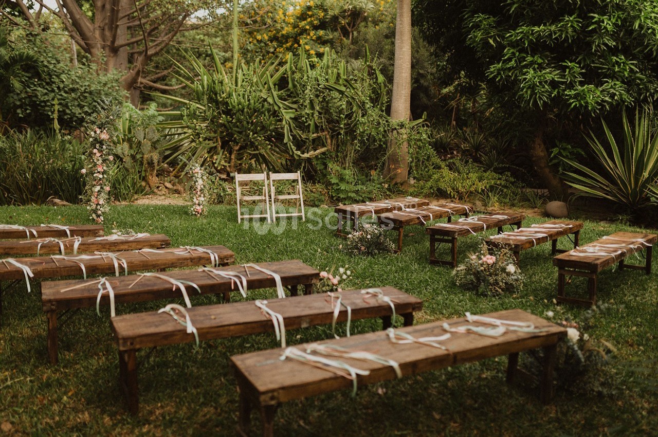 Bancs en bois disposés sur une pelouse pour une cérémonie en plein air, entourés de végétation et de fleurs.
