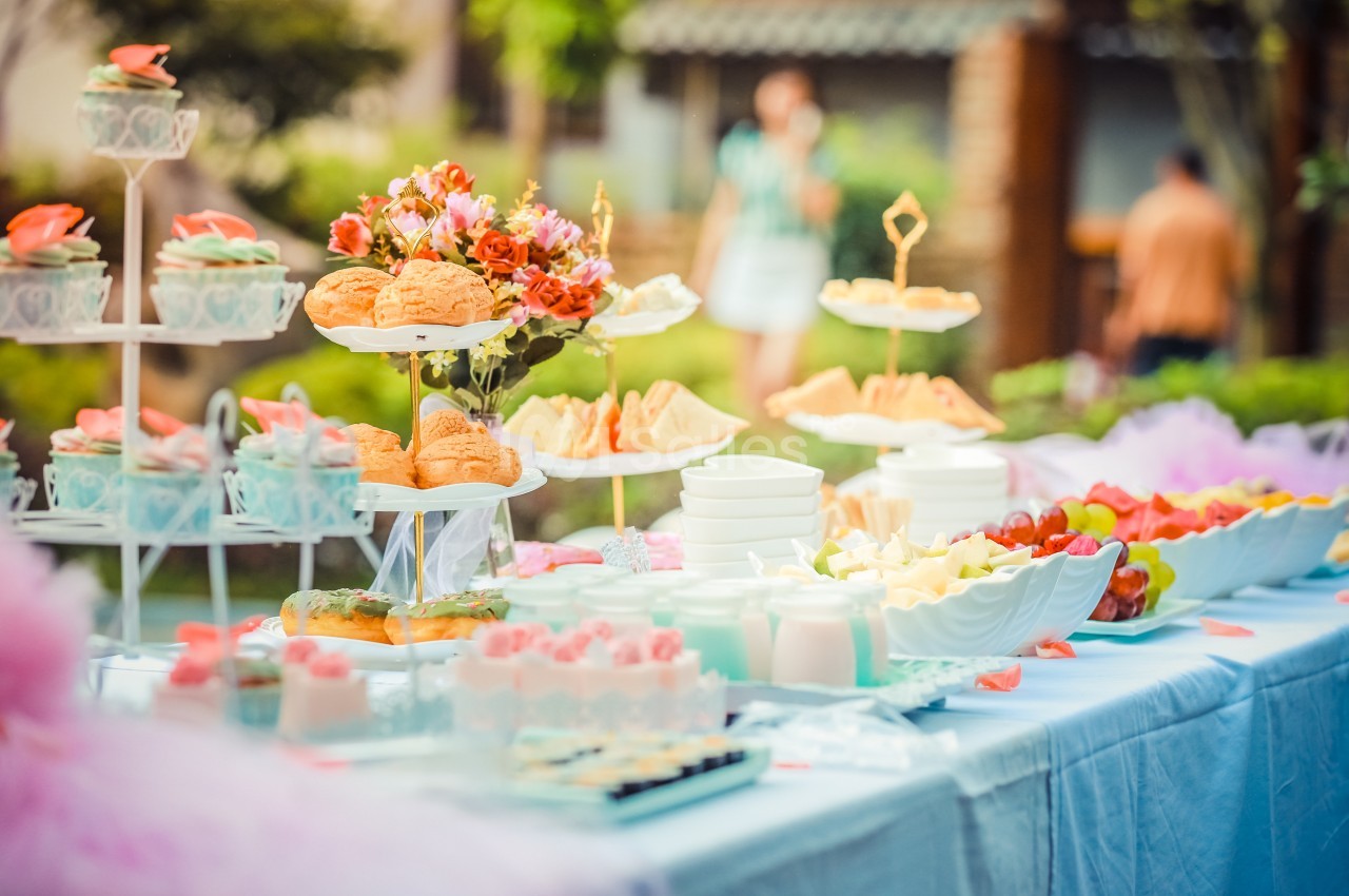 Table dressée en extérieur avec des pâtisseries, fruits, sandwiches et décorations florales.