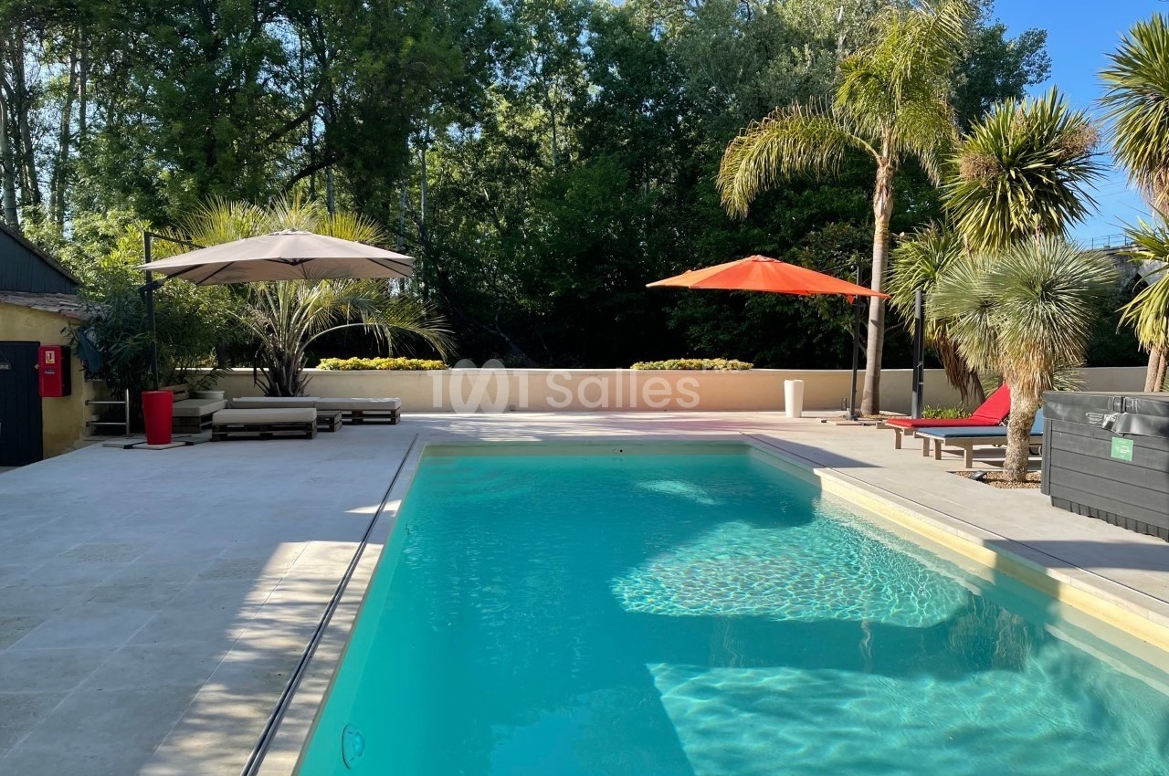 Piscine extérieure entourée de transats, parasols et végétation, sous un ciel dégagé et ensoleillé.