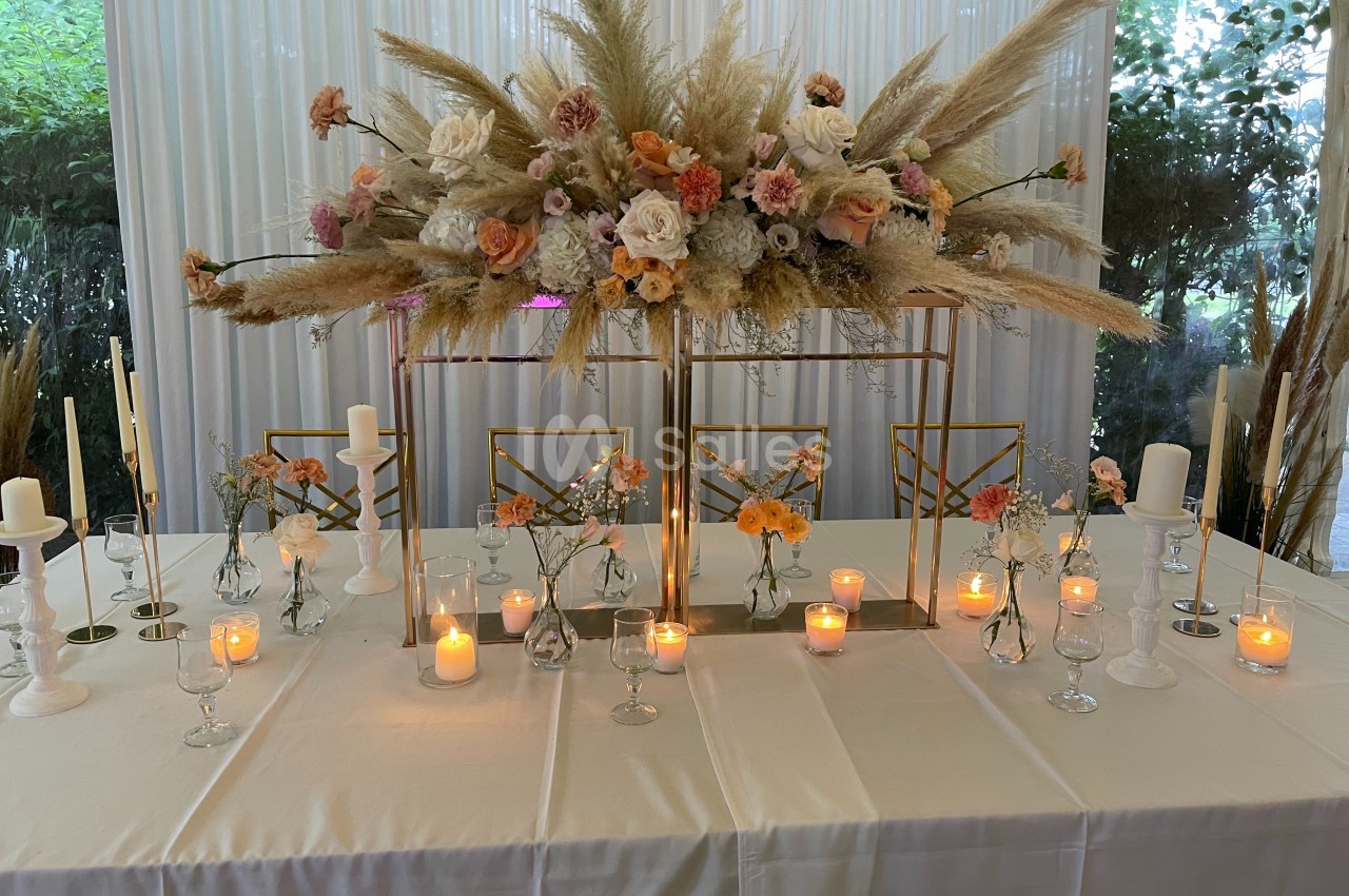 Table décorée avec des bougies allumées, des fleurs séchées et fraîches dans des vases, sur fond de rideaux blancs.