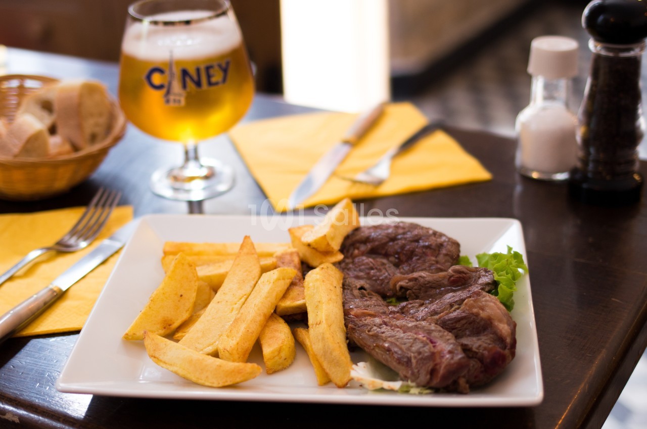Assiette contenant un steak grillé, des frites et de la salade, servie sur une table avec une bière et des couverts.