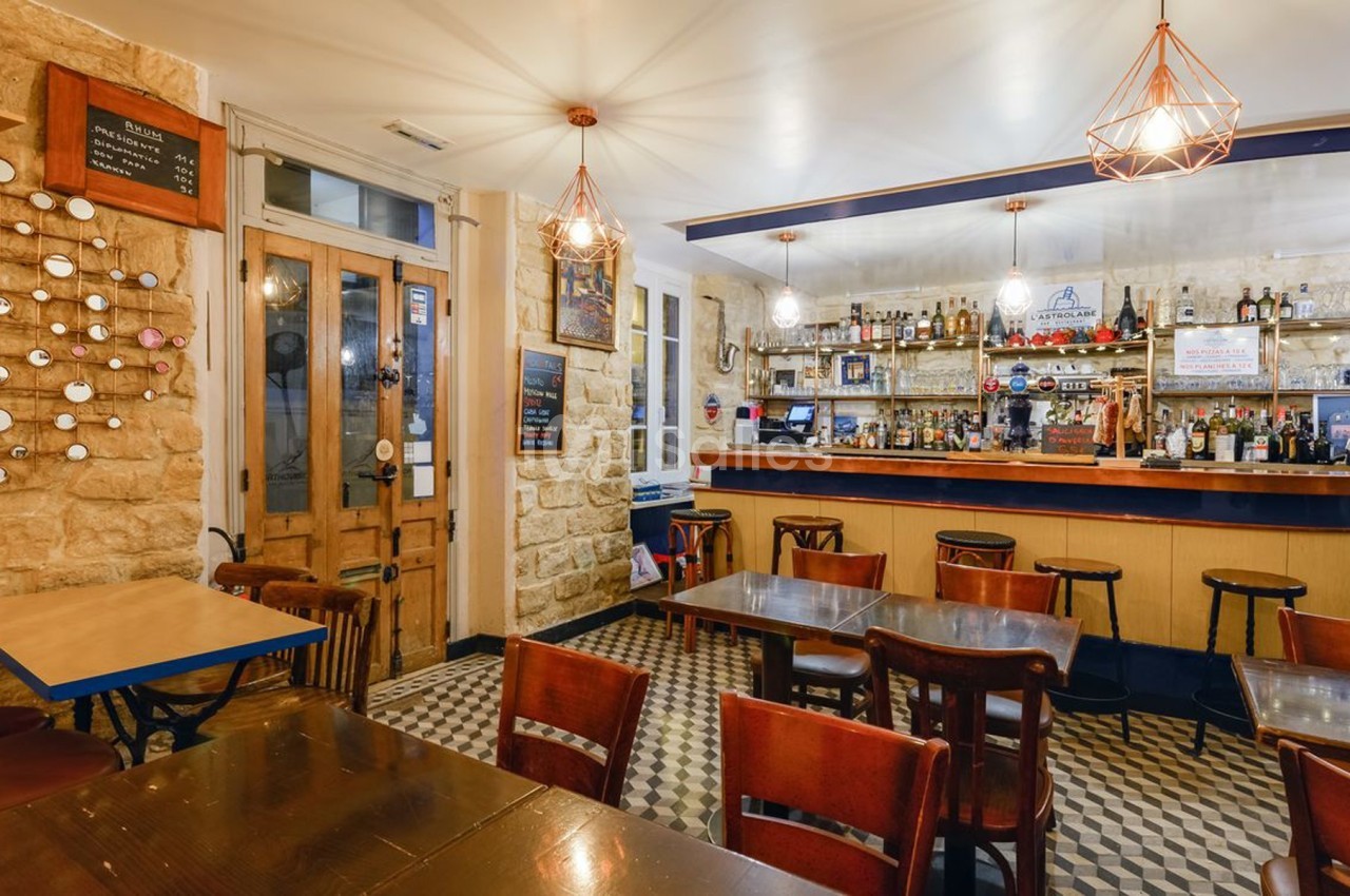 Intérieur d'un café avec tables en bois, chaises, bar en arrière-plan et décoration murale en pierre apparente.