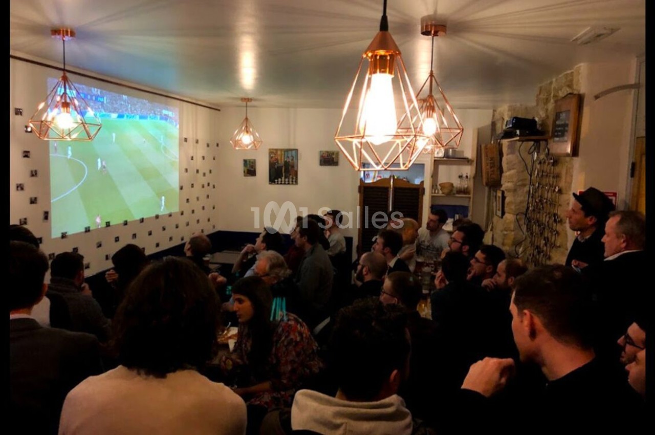 Des personnes rassemblées dans un bar regardent un match de football projeté sur un écran mural.