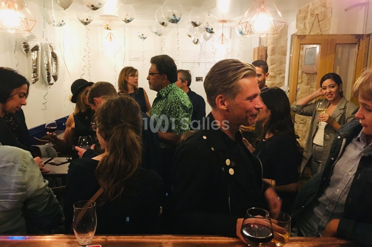 Groupe de personnes discutant dans un bar décoré avec des ballons et des guirlandes, ambiance conviviale.