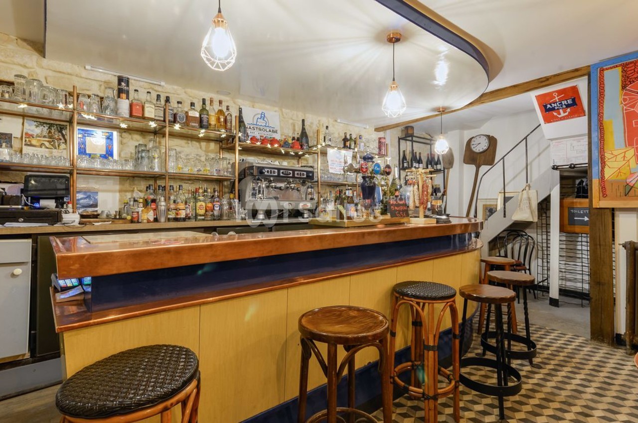 Bar avec comptoir en bois et cuivre, tabourets hauts, étagères remplies de bouteilles et éclairage suspendu.