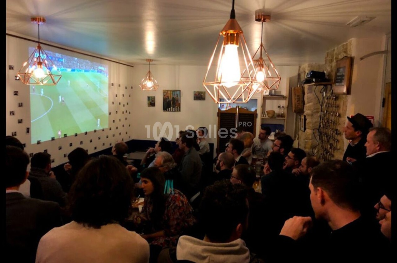 Des personnes rassemblées dans un bar regardent un match de football projeté sur un écran mural.