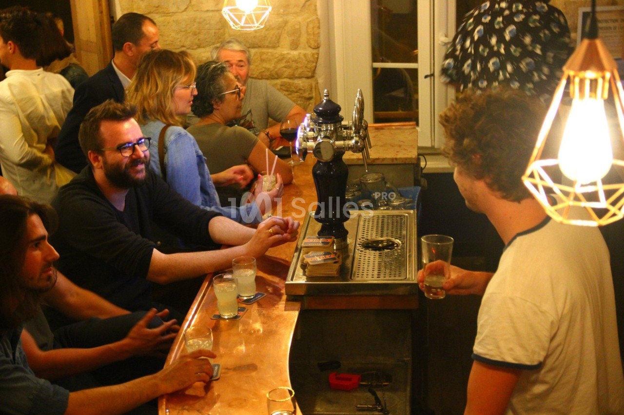 Des personnes discutent et boivent autour d'un comptoir de bar éclairé par des lampes suspendues.
