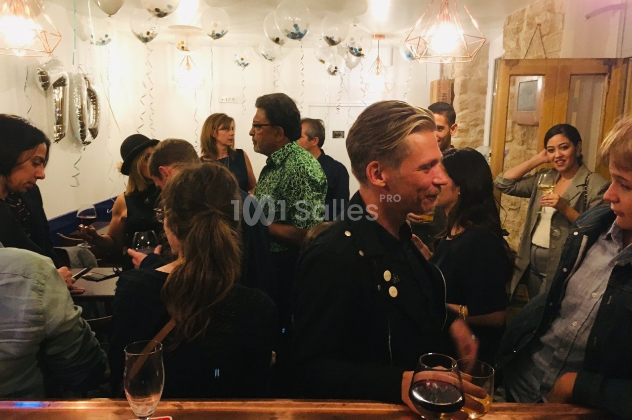 Groupe de personnes discutant dans un bar décoré avec des ballons et des guirlandes, ambiance conviviale.