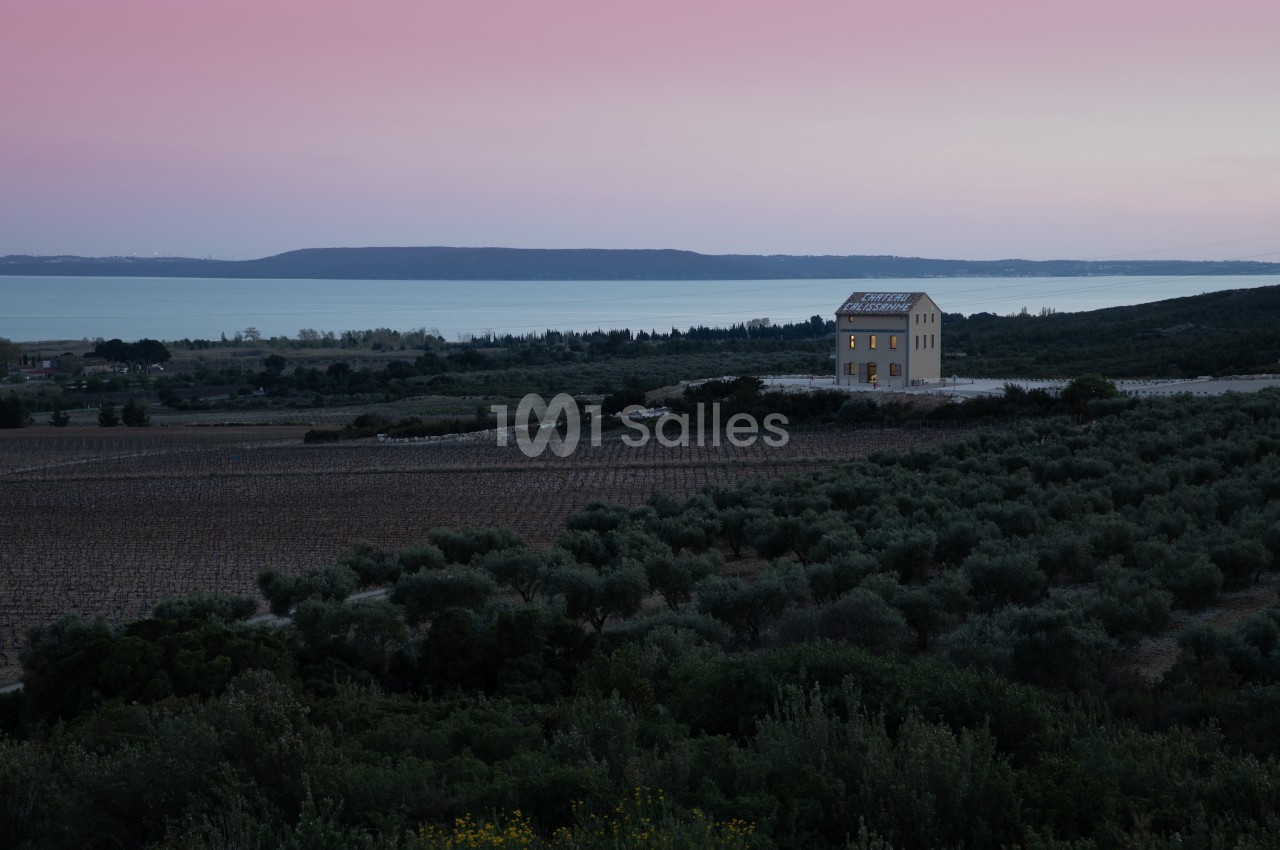 Maison isolée entourée de champs et d'oliviers, avec vue sur un lac au coucher du soleil.