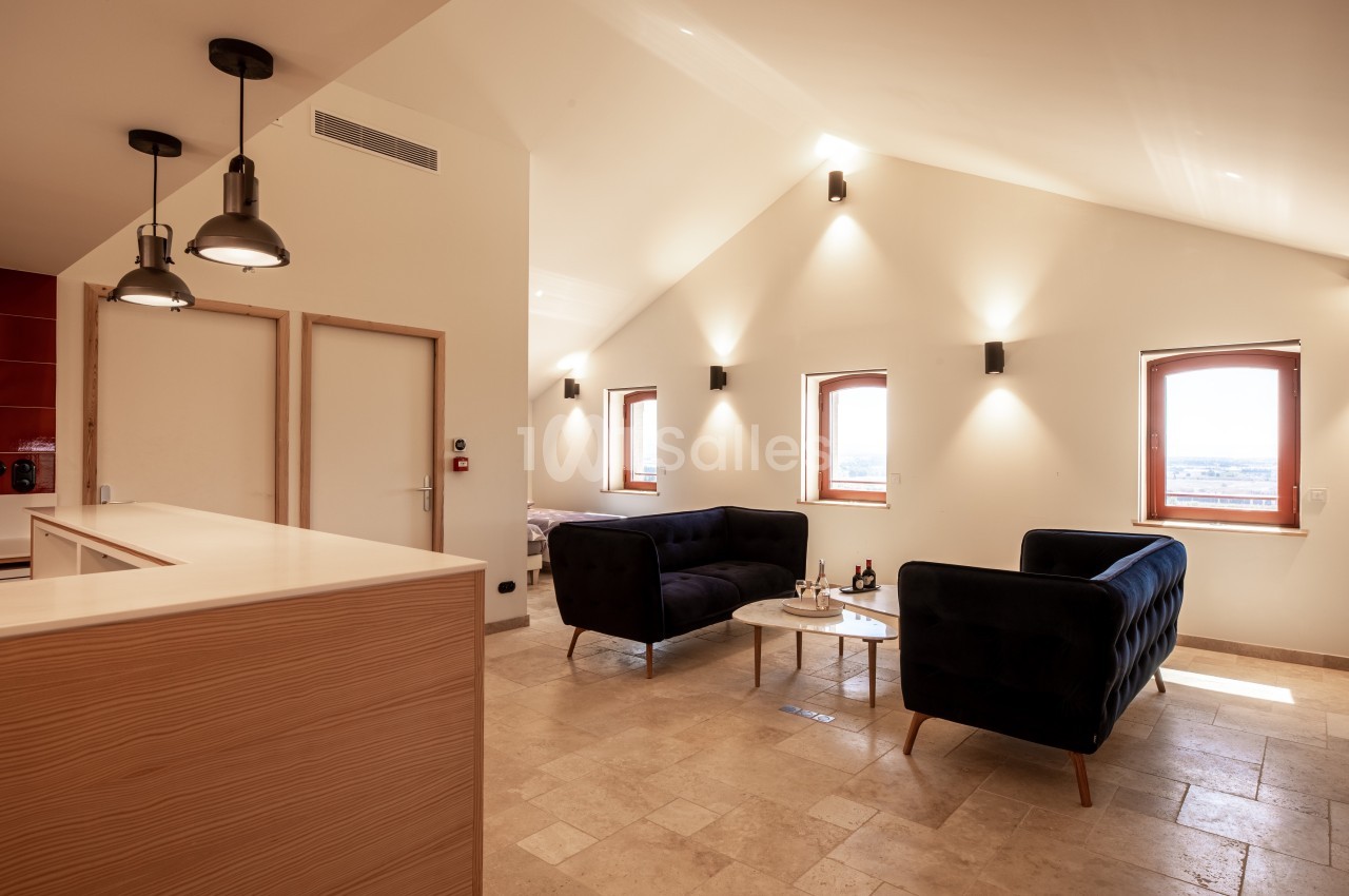Salon lumineux avec deux canapés noirs, une table basse, des murs blancs et des fenêtres laissant entrer la lumière…