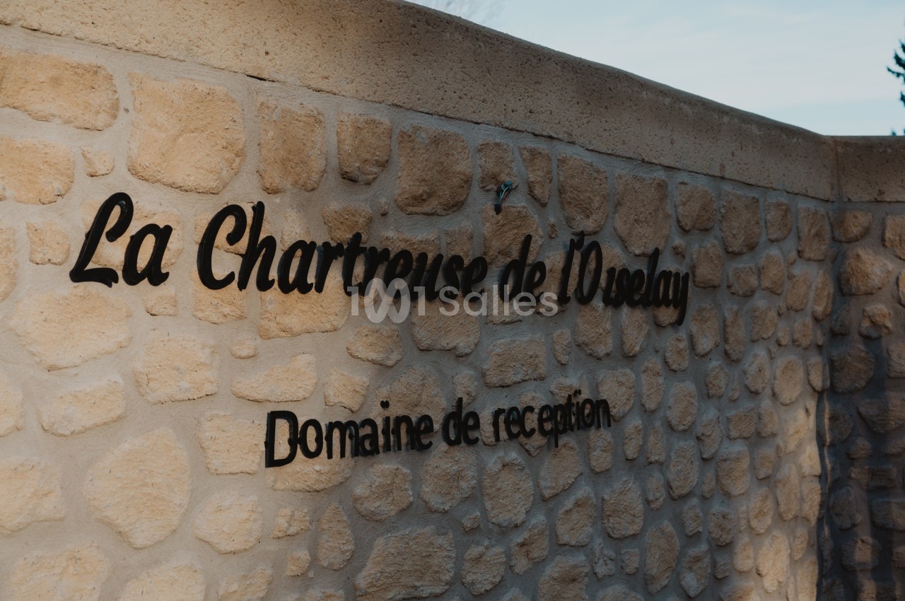 Mur en pierre avec l'inscription ’La Chartreuse de l'Oréalay, Domaine de réception’ en lettres noires.