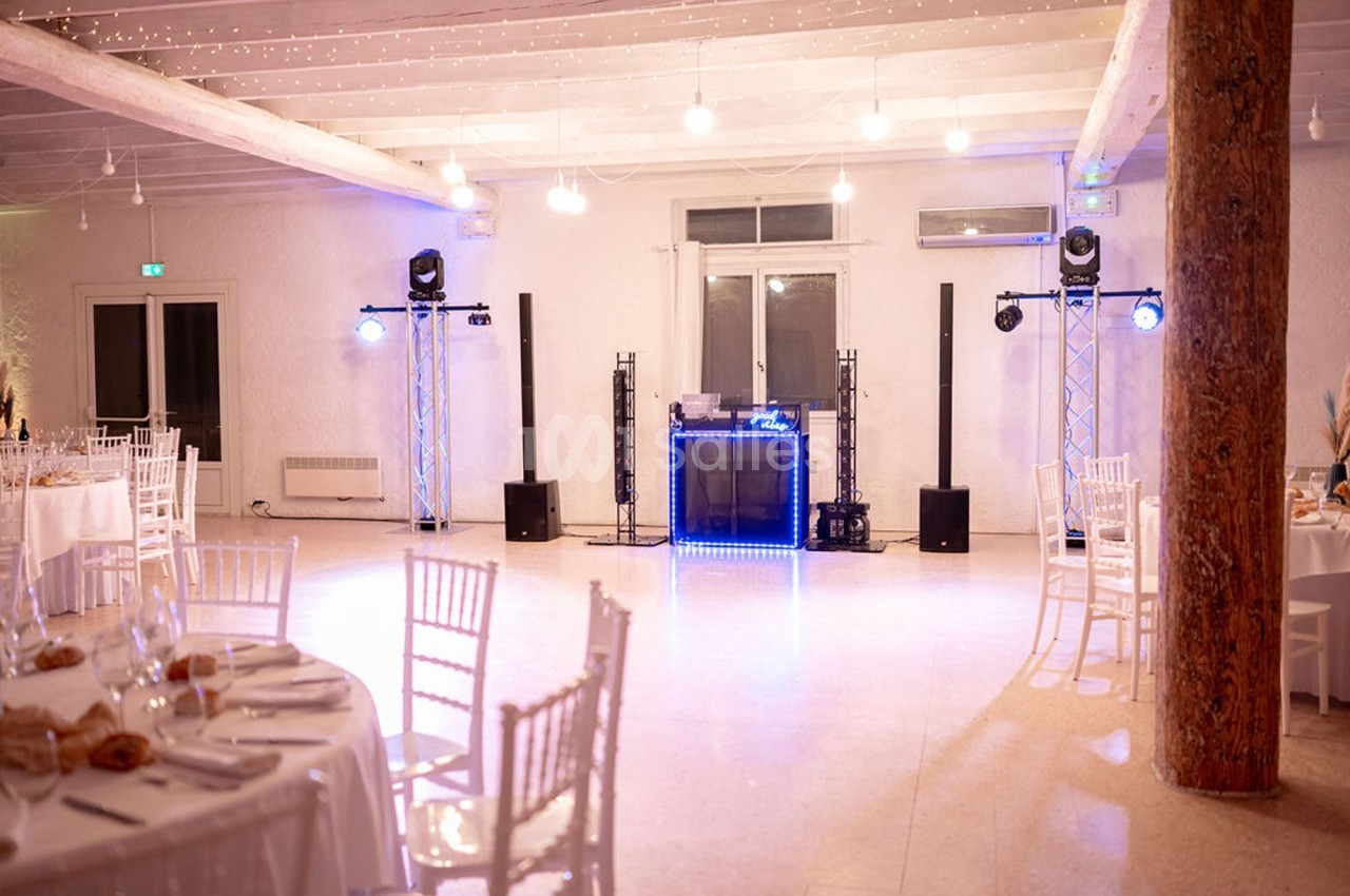 Salle de réception lumineuse avec tables dressées et espace central équipé pour une animation musicale.