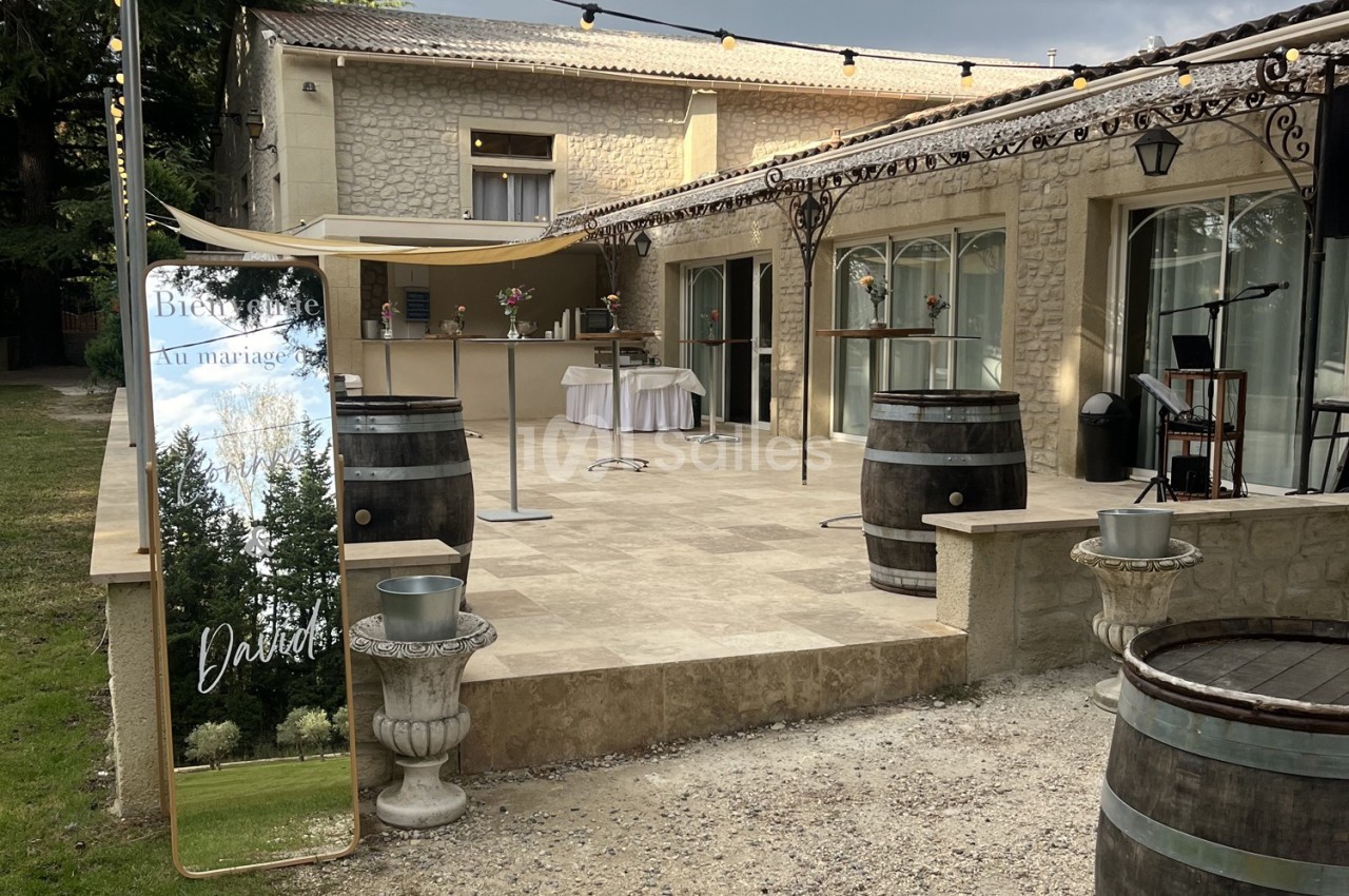 Terrasse en pierre avec décorations de mariage, tonneaux en bois, miroir de bienvenue et guirlandes lumineuses.