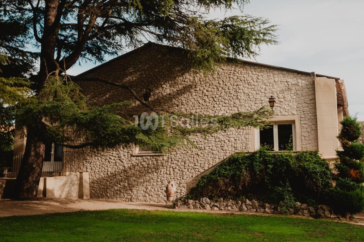 Façade en pierre d'une maison entourée d'arbres, avec une pelouse au premier plan.
