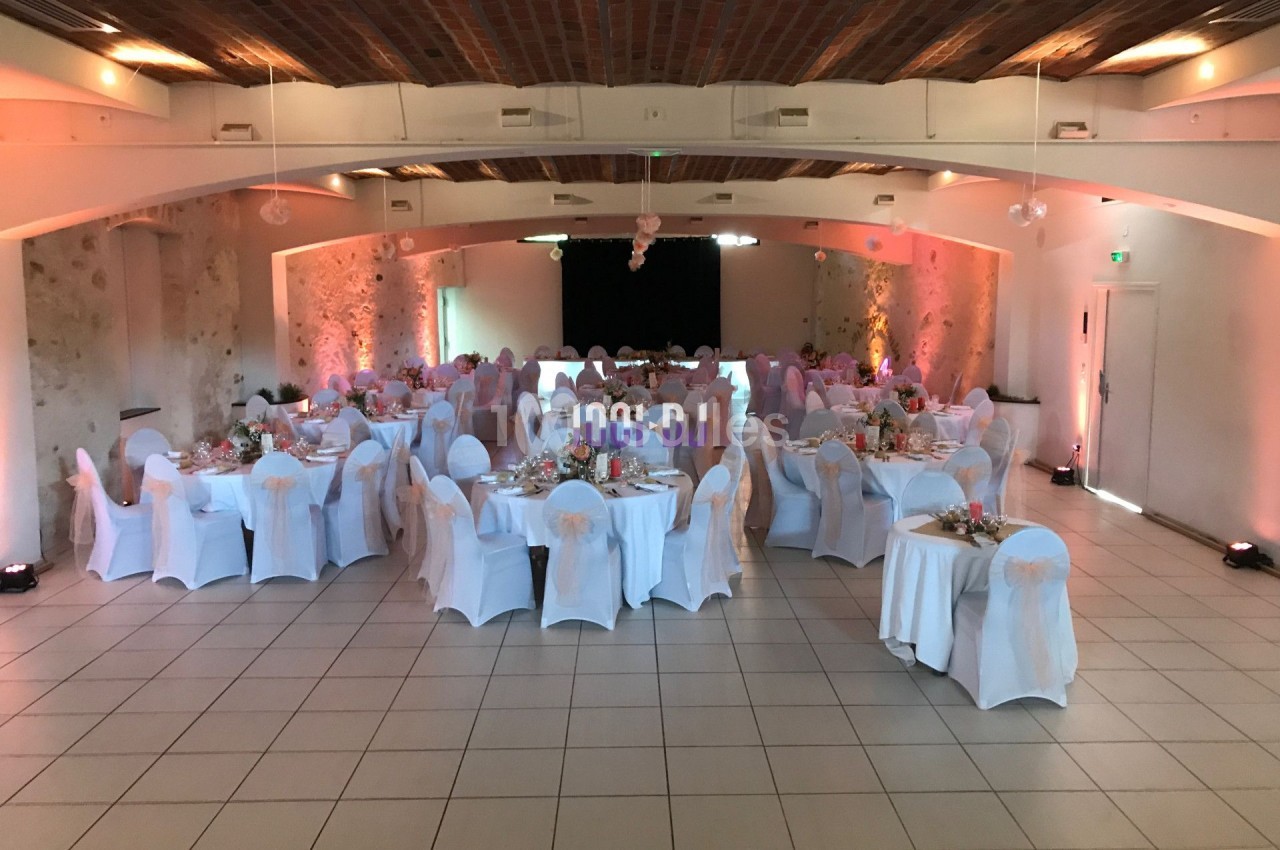 Salle de réception décorée avec des tables rondes, nappes blanches et chaises habillées, prête pour un événement.