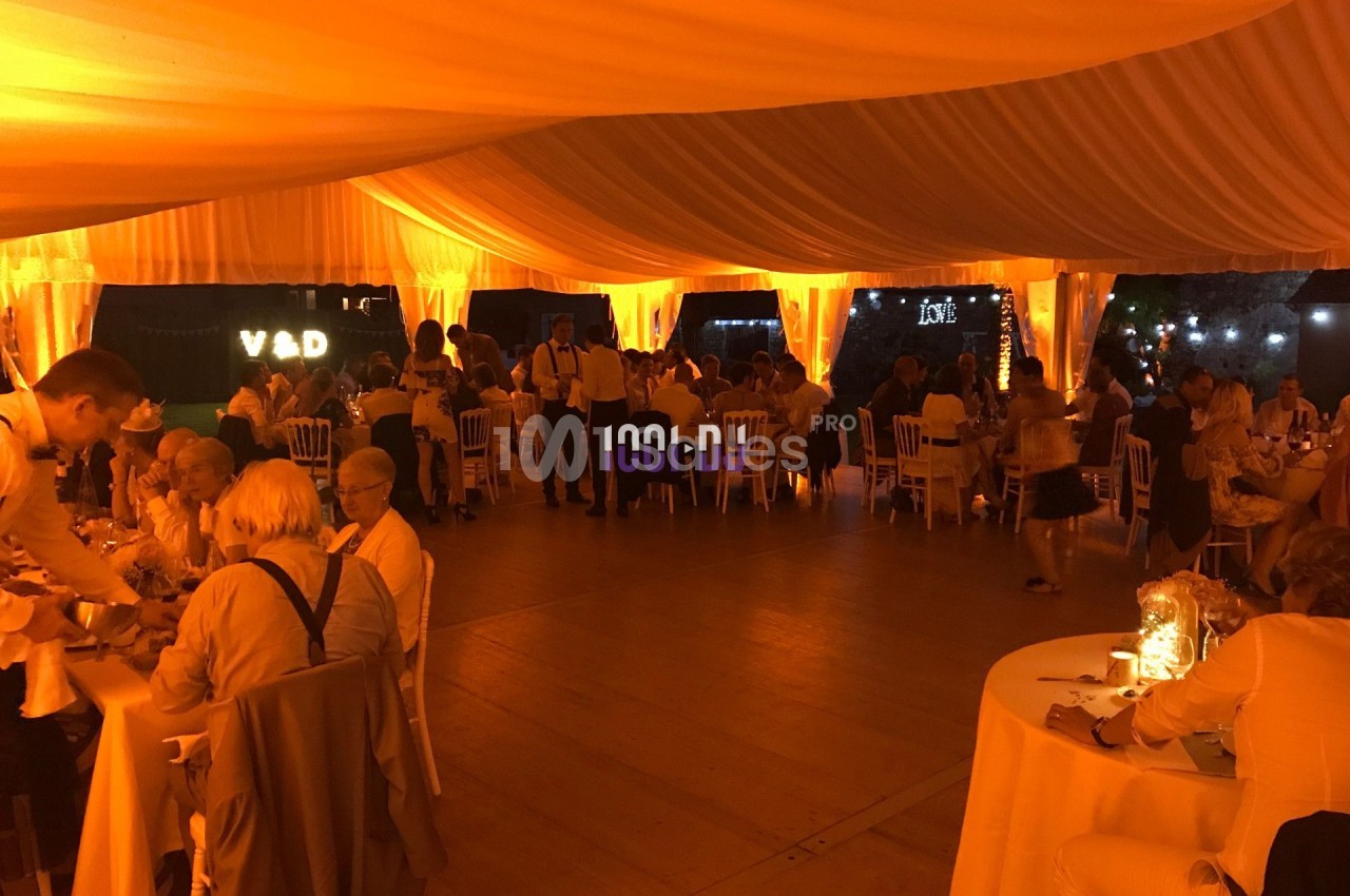Salle de réception éclairée en orange avec des invités assis à des tables rondes sous une grande tente.
