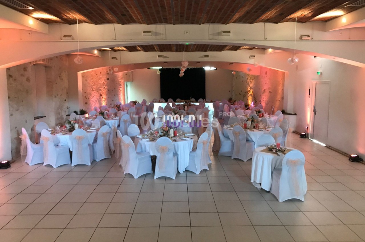 Salle de réception décorée avec des tables rondes, nappes blanches et chaises habillées, prête pour un événement.