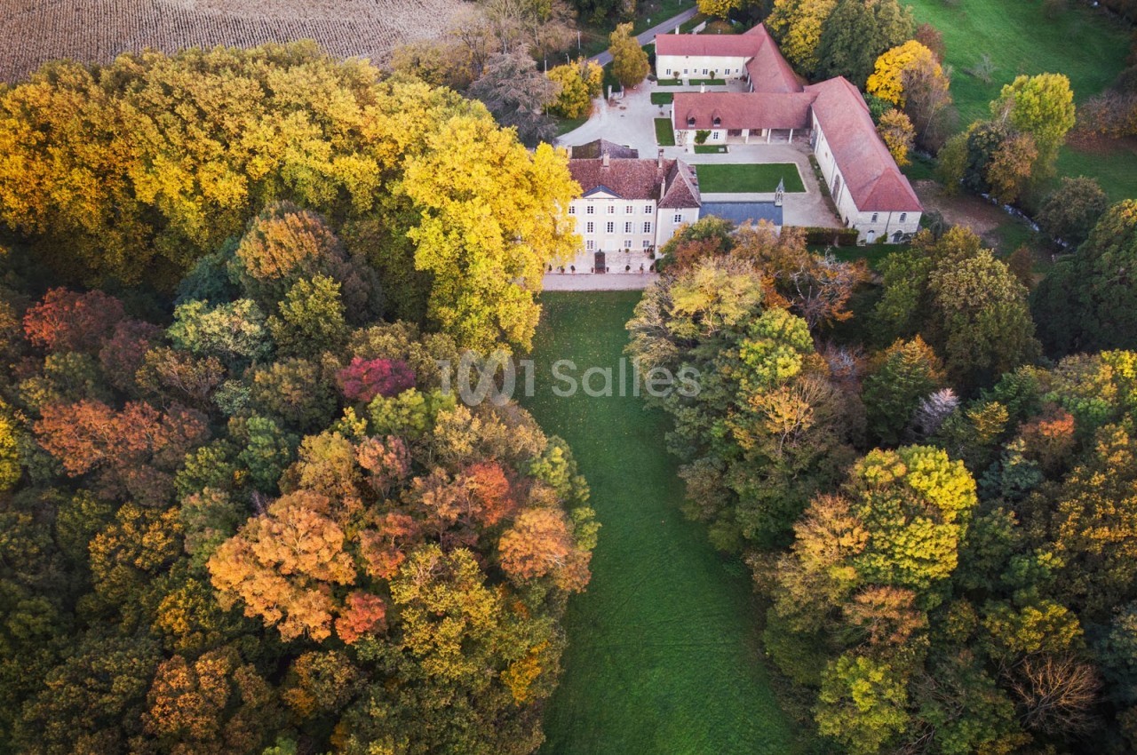 Vue aérienne d'un domaine entouré de forêts aux couleurs automnales, avec bâtiments et pelouse centrale.