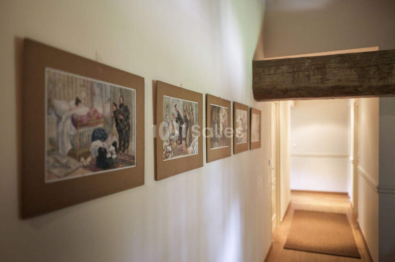 Couloir éclairé avec des cadres illustrés accrochés au mur, poutre en bois apparente au plafond.